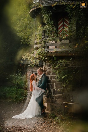 In Germany's Märchenwald Altenberg in Odenthal, the wedding couple poses for a dreamy, filter-enhanced portrait beside a stone tower within the atmospheric fairy-tale forest.